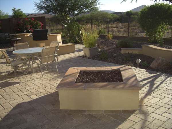 A desert backyard with a large manufactured brick floor connecting the outdoor kitchen, patio, and firepit.