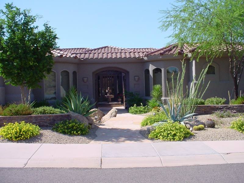 A well balanced front yard design with stone walls and shrubs welcome visitors to a beautiful courtyard entrance with a fountain. 