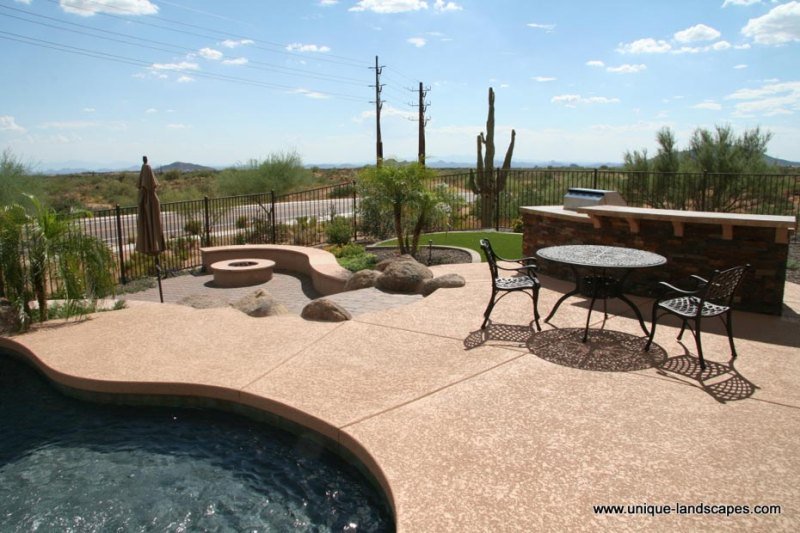 Poolside patio with an outdoor kitchen and lower level firepit surrounded by natural desert plants.